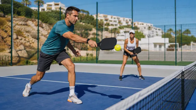 Jugador de pickleball flexionado junto a la línea de la pista con la pelota perforada en primer plano